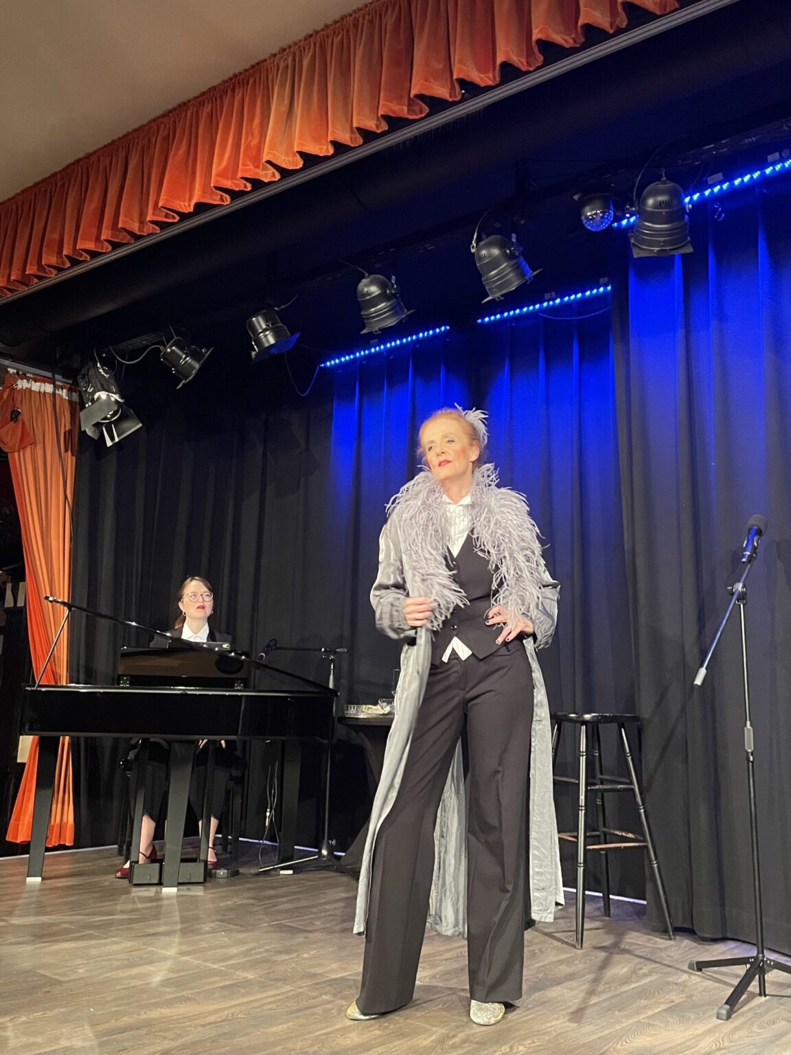 Marie Oser als Zeitreisende und Sophie Sczepanek am Klavier vor blauem Bühnenvorhang