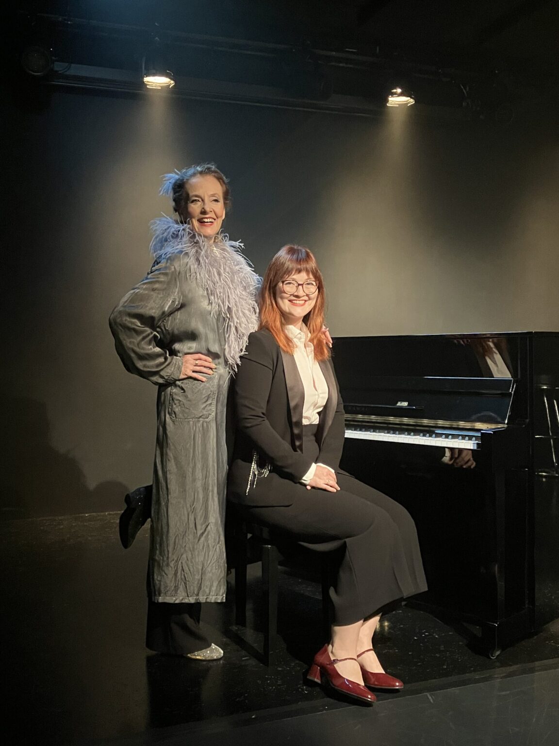 Marie Oser im silbergrauen Seidenmantel mit Straussenfederboa, links stehend, neben der Pianistin Sophie Sczepanek, sitzend, vor dem Flügel ©