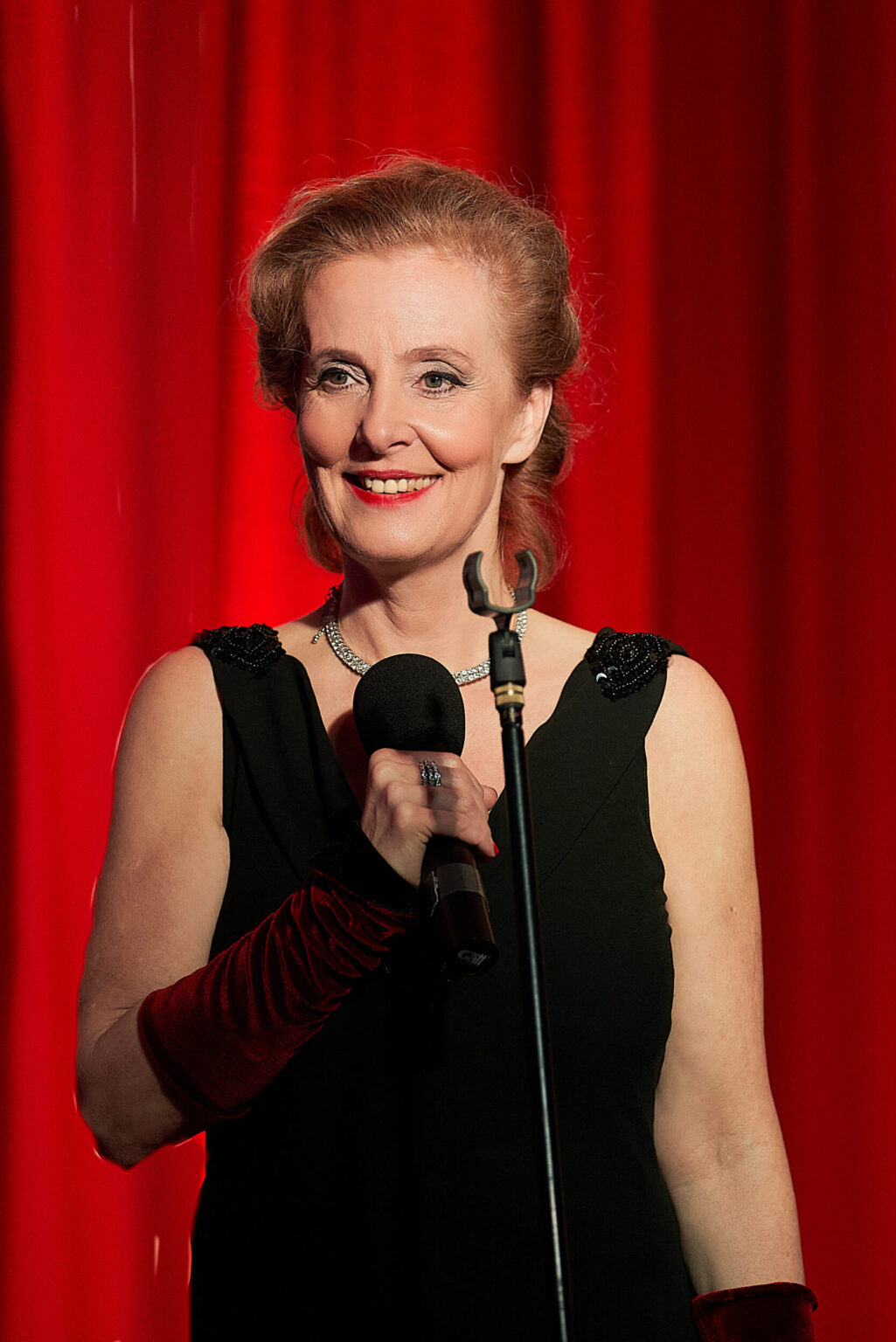 Marie Oser mit Mikro und schwarzem Kleid vor rotem Vorhang