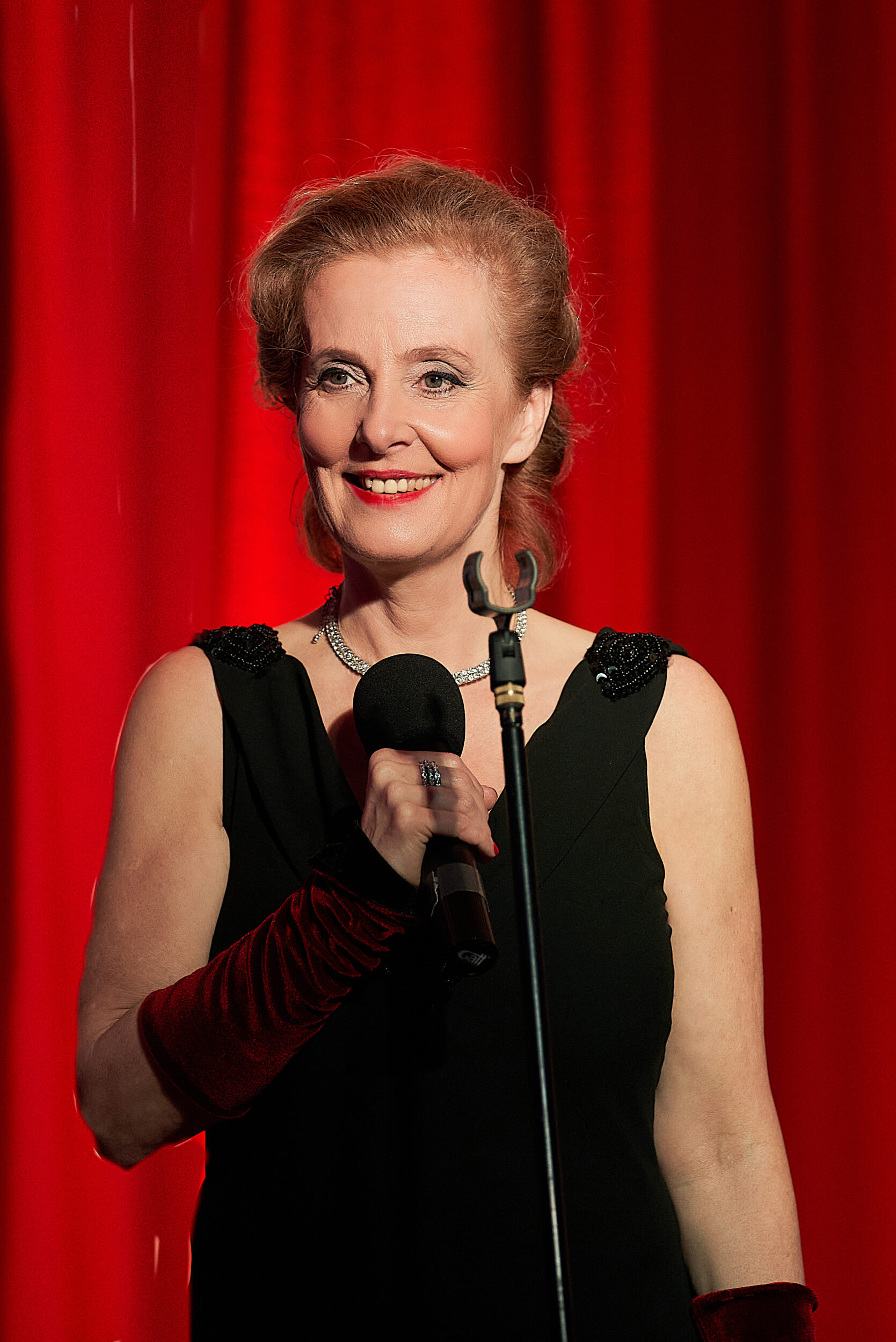 Marie Oser mit Mikro und schwarzem Kleid vor rotem Vorhang